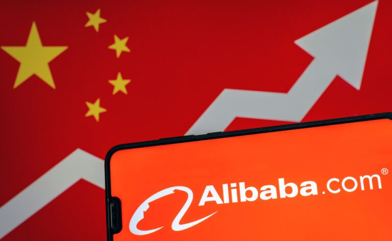 Logo společnosti Alibaba zobrazené na mobilním telefonu. V pozadí čínská vlajka, růst akcie Baba