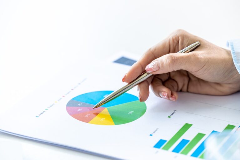 Ženská ruka drží propisku, a ukazuje na barevný koláčový graf. Koncept jak diverzifikovat portfolio