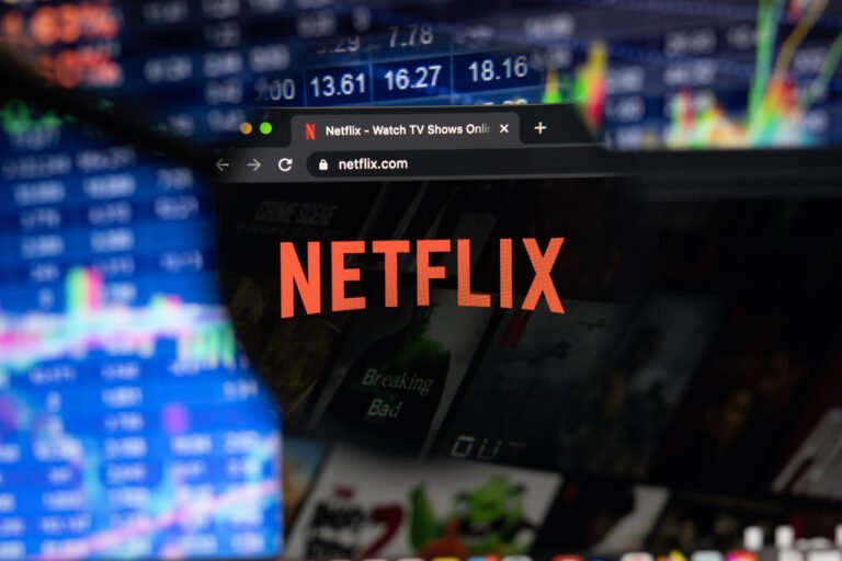 lupa zamerena na logo streamovaci spolecnosti netflix a v pozadi grafy a hodnoty akcii