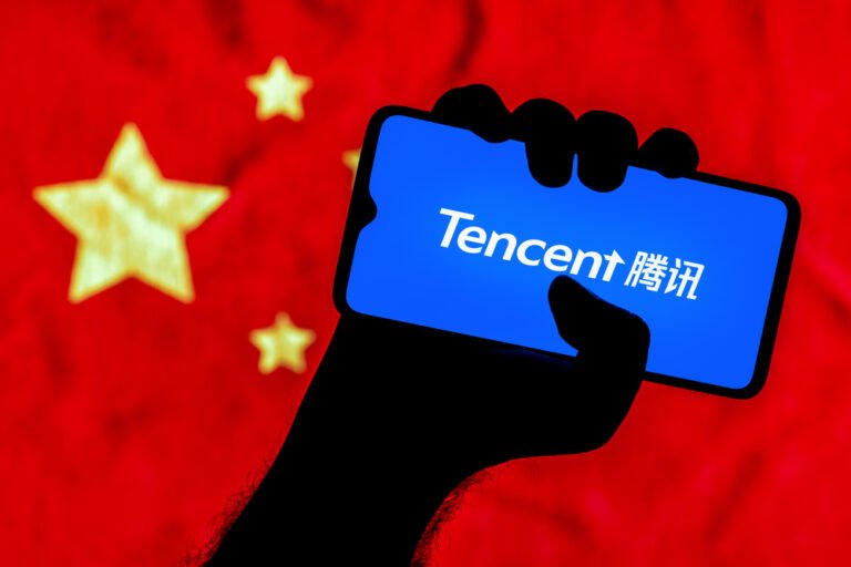 Chytrý telefon s logem společnosti Tencent v sevřené ruce a v pozadí je čínská vlajka
