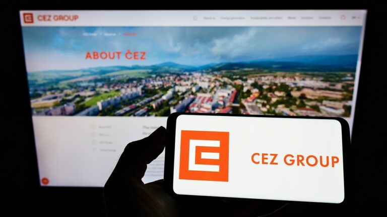 Osoba držící chytrý telefon s logem české energetické společnosti ČEZ, v pozadí monitor