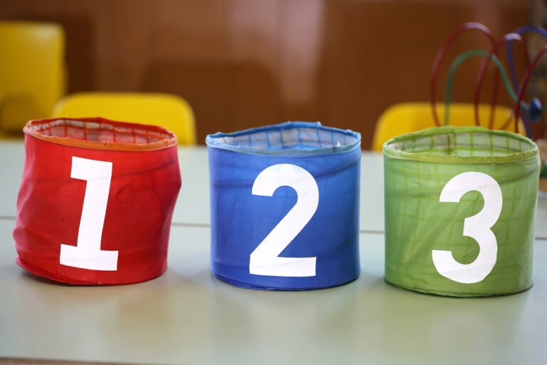 tři barevné sklenice s nakreslenými čísly 1 2 3 na školní lavici