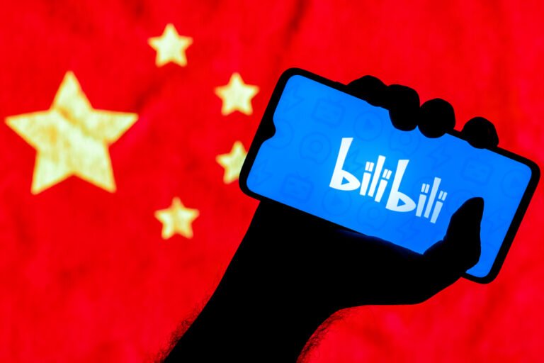 V pozadí je čínská vlajka, v ruce je držen chytrý telefon a na ní je logo společnosti Bilibili, Bilibili čínská webová stránka pro sdílení videí zaměřená na animace, komiksy a hry