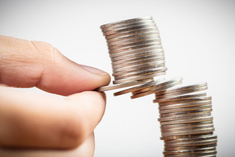 Detailní záběr na prsty, které se snaží vytáhnout některé mince z hromádky a riskují, že se hromádka mincí zhroutí, koncept investičních chyb