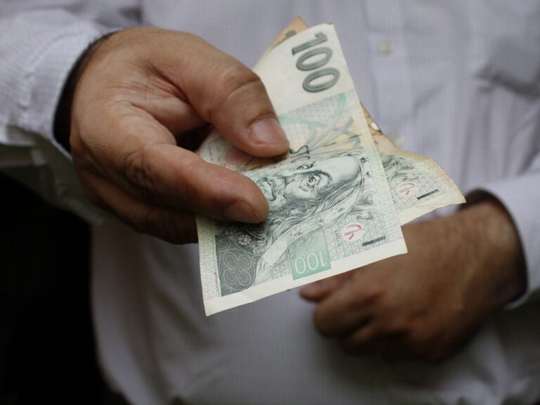 Ruka muže držícího české bankovky v hodnotě 100 korun