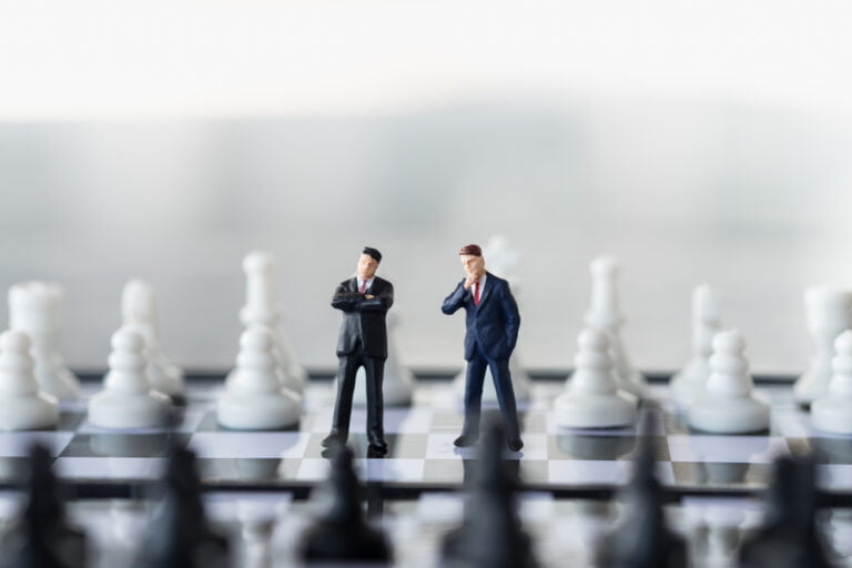 Miniturní figurky dvou podnikatelů na šachovnici. Koncept změny investiční strategie