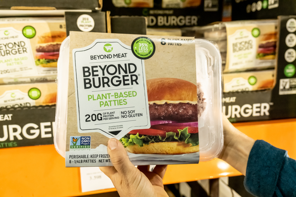 Ruka držící balení rostlinného hamburgru značky Beyond Meat, akcie Beyond Meat