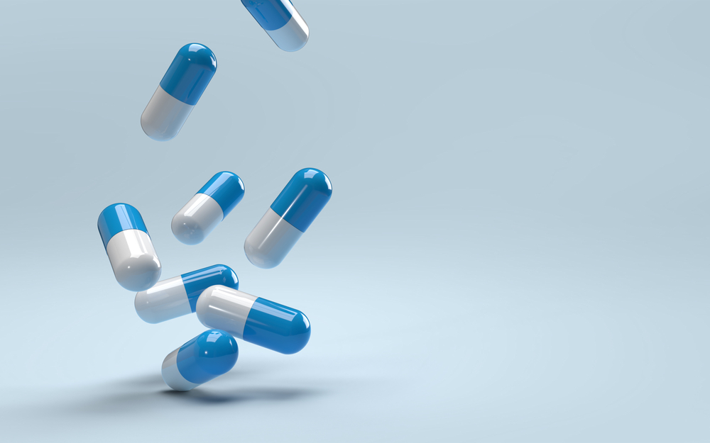 Padající pilulky na modrém pozadí, antibiotika. Koncept vývoje léků, akcie Eli Lilly