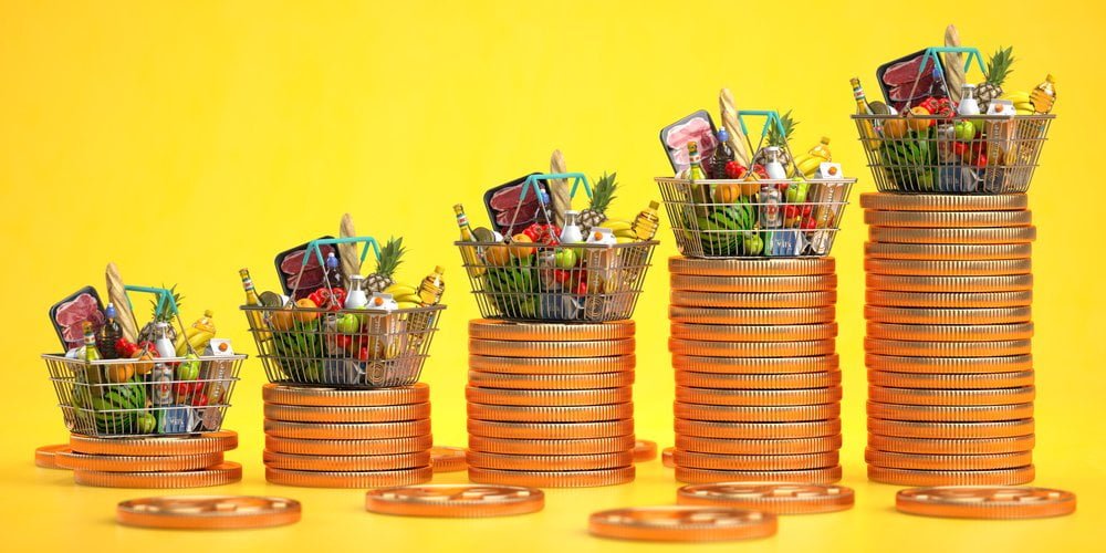 Nákupní košíky s potravinami na hromadě mincí na žlutém pozadí, koncept rostoucí inflace a zdražování potravin, investice proti inflaci
