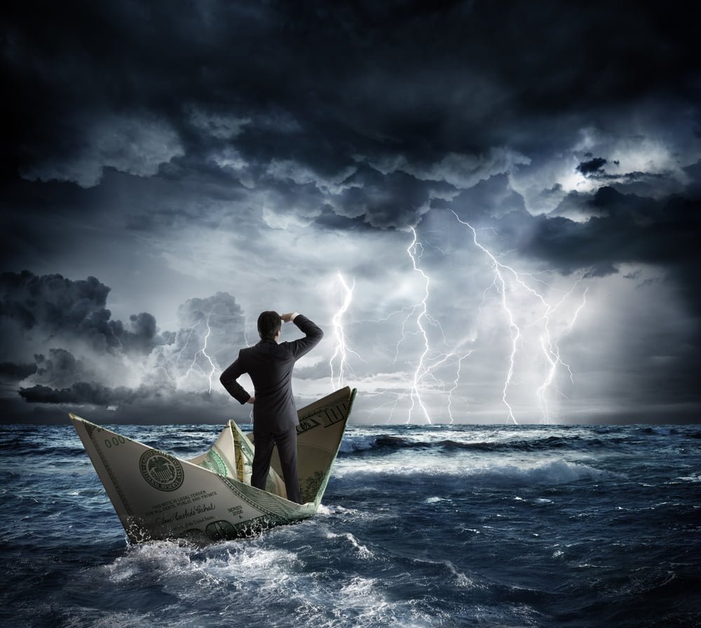 Muž v obleku na loďce pluje na rozbouřeném moři, a rozhlíží se. Koncept: Do čeho investovat v době krize? 