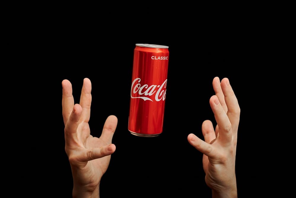 Ruce chytající plechovku Coca Coly na černém pozadí. Koncept akcie Coca Coly a její růst