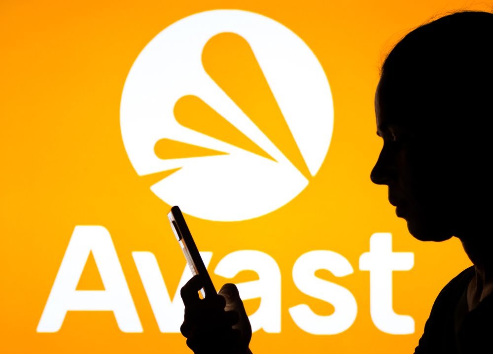 Na této fotografii je logo společnosti Avast a v pozadí je silueta ženy držící mobilní telefon. Koncept akcie Avastu a její stažení z burzy