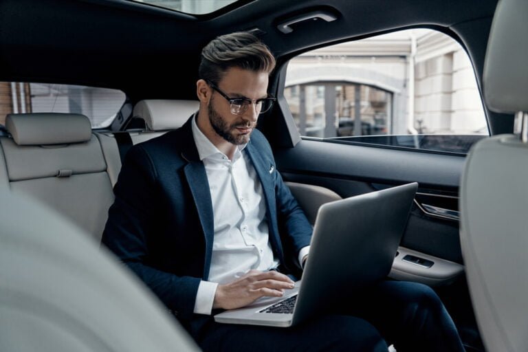 Mladý muž v obleku pracuje na notebooku, zatímco sedí v autě