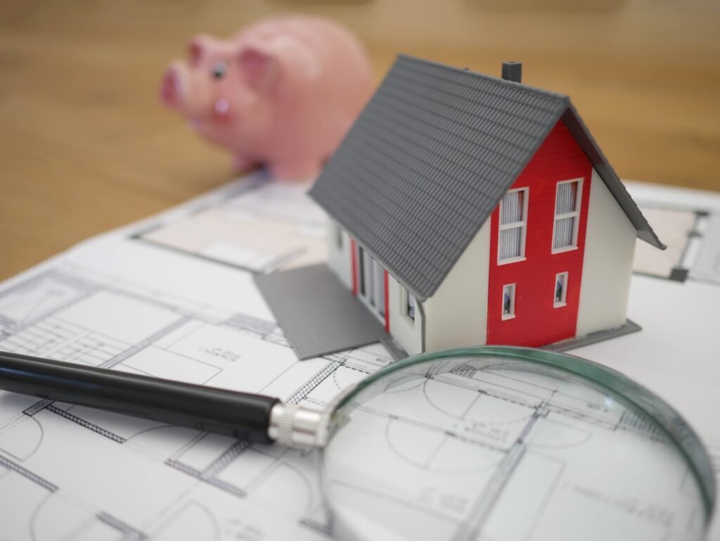 Model domu, lupa na výkresu a v pozadí je růžové prasátko. Koncept: nejlepší dividendové akcie (REIT) 